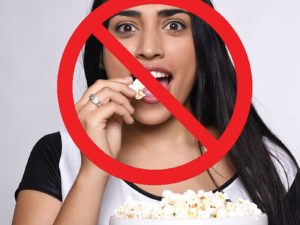 Image of teen eating popcorn. A big red cross is overlaid to indicate-do not eat popcorn when wearing braces