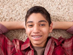 Milton Orthodontics Teen Male, relaxing on the carpet, smiling with metal braces   